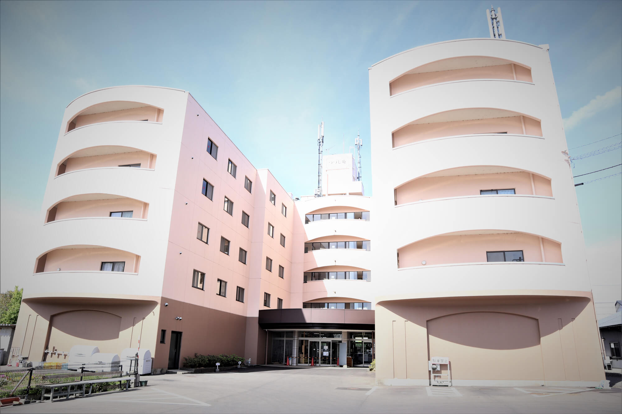 モダンデザインの介護施設建物。曲線的な白とピンク色の外観が特徴的な多階層構造。
